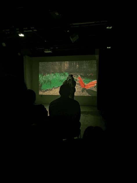 A dark screening room: silhouettes of the audience watching the projected headset view of the VR grove